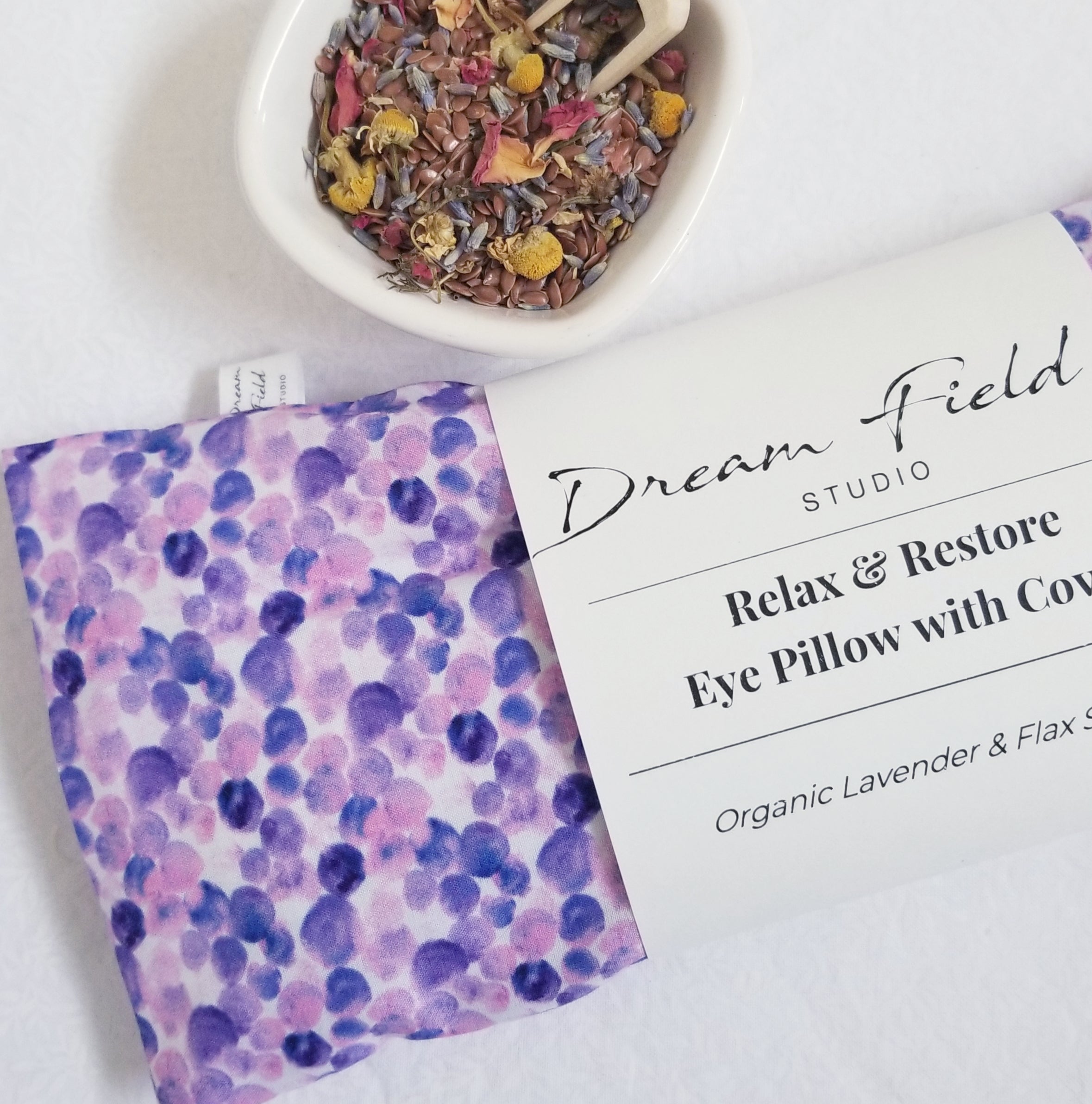 Organic lavender eye pillow with purple dot cotton cover and white bowl filled with herbs