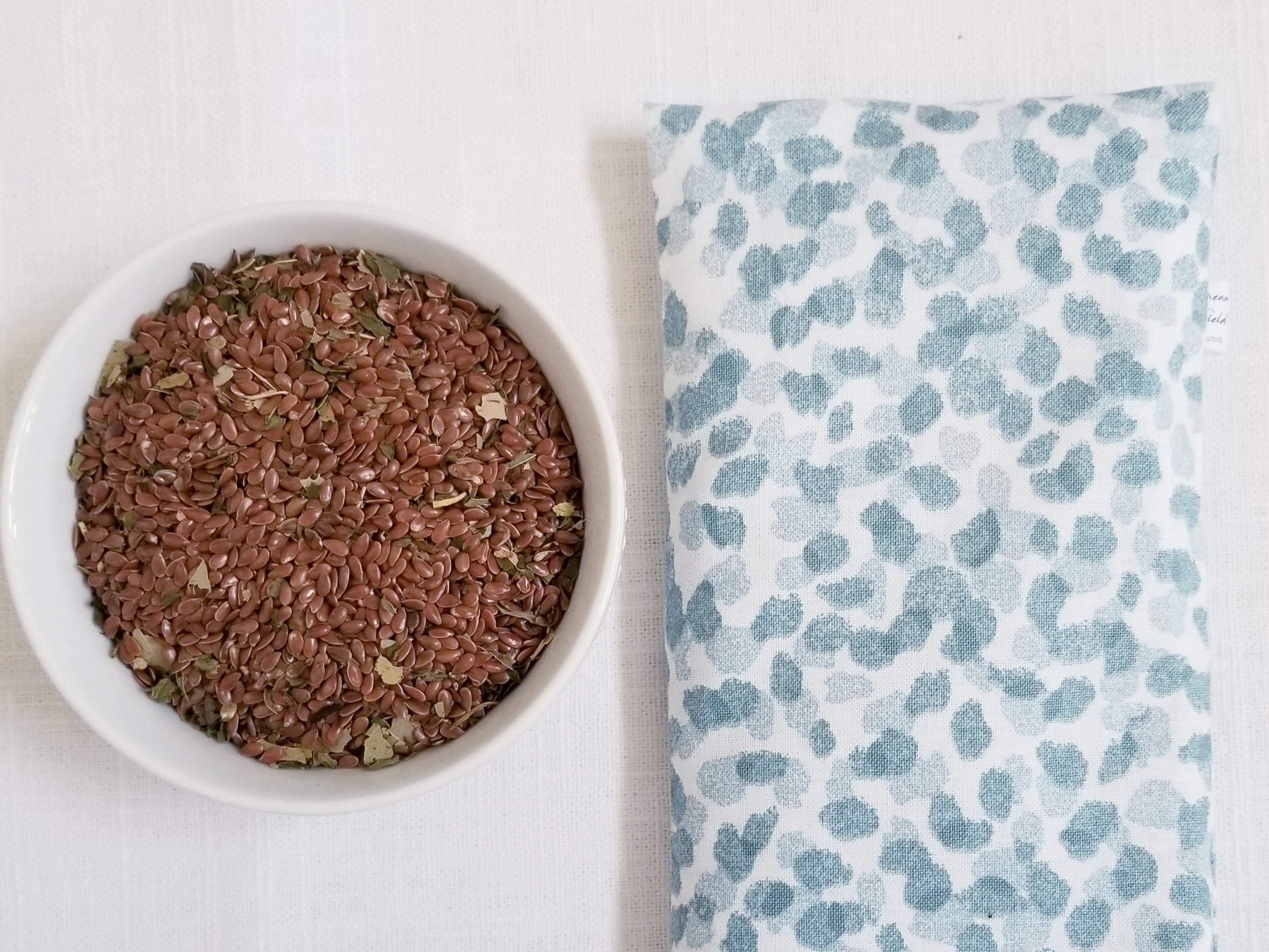 Closeup of blue spa dot print fabric and bowl of flax seeds and organic herb leaves